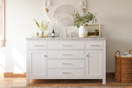 White vanity with marble top and chrome hardware, styled with round mirror and soft neutral accents.