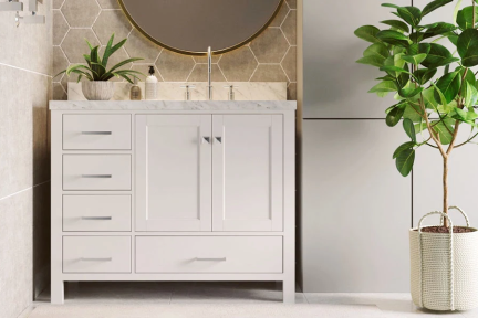 White vanity with marble top and nikel hardware, styled with round mirror, plant, and beige tile walls.